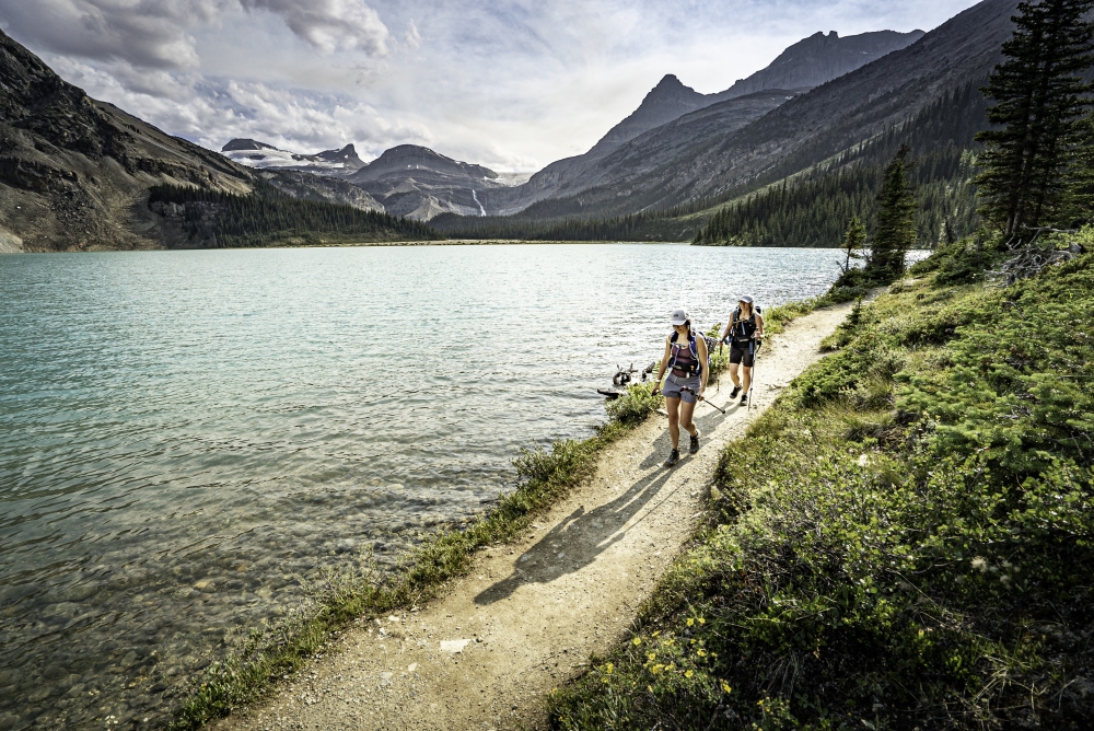Two people hiking down a path in Alberta Canada by Bow Lake during the day in summer with mountains in the distance