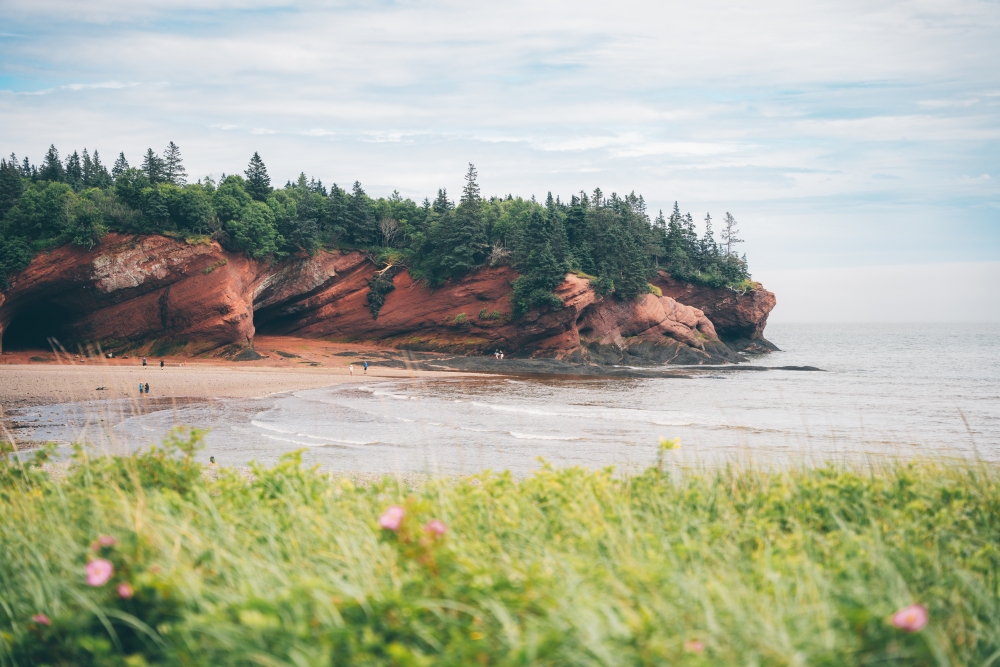 View of St Martin's New Brunswick Canada during the day with the beach, rock formations, grass and trees
