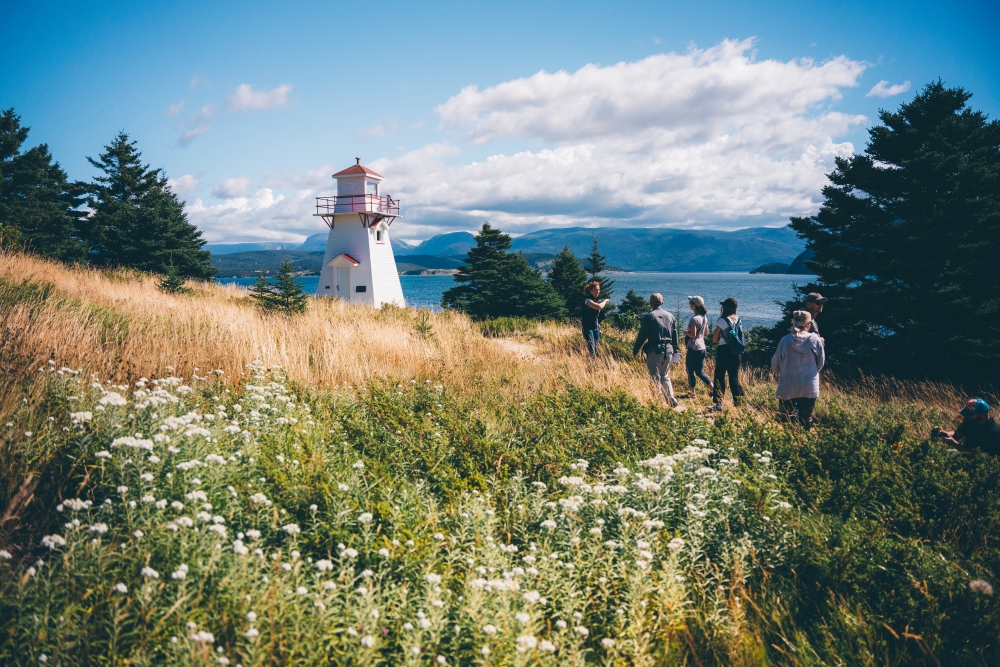 People walking outside at Woody Point Lighthouse in Newfoundland Canada during the day in summer by the ocean 