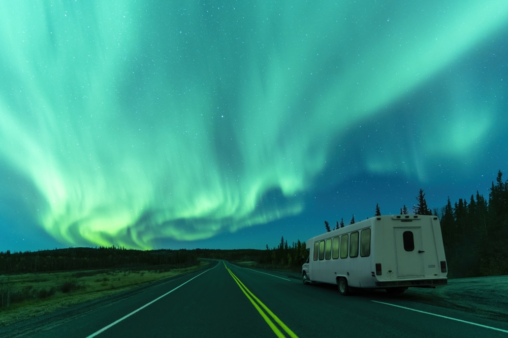 View of the Auroras in the sky during fall at night in Yellowknife Northwest Territories Canada outside with a bus driving down the open road