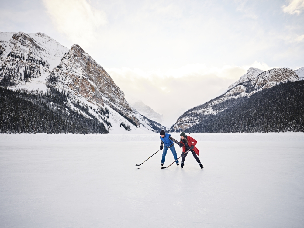 Two people wearing skates and a blue and red jacket playing hockey on the frozen ice at Lake Louise Alberta Canada in the winter during the day