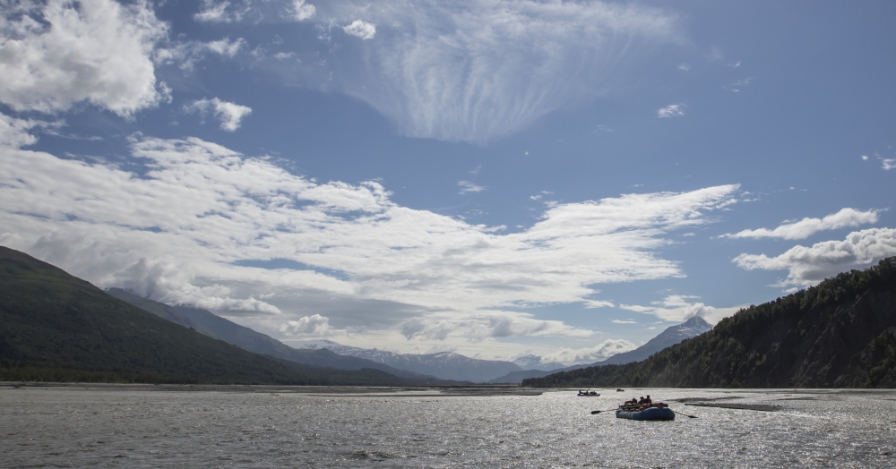 View of the water outside during the day in British Columbia Canada with people rafting and mountains in the distance with blue skies